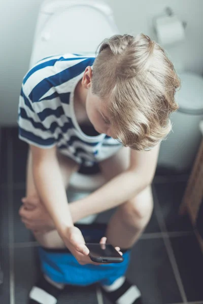 Ragazzo adolescente seduto su un water con il suo cellulare — Foto Stock