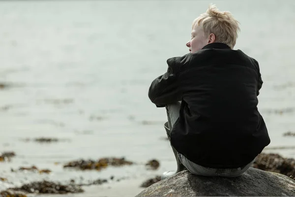 Junge schaut im Sitzen auf Felsbrocken zur Seite — Stockfoto