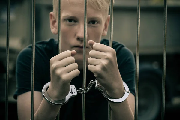 Handcuffed teenage boy behind bars — Stock Photo, Image