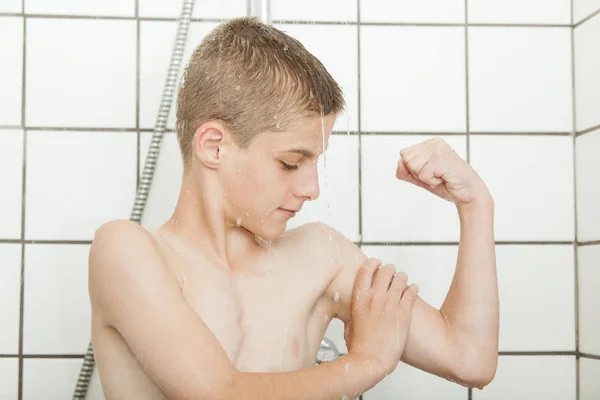 Joven niño sintiendo su propio bíceps mientras se ducha — Foto de Stock