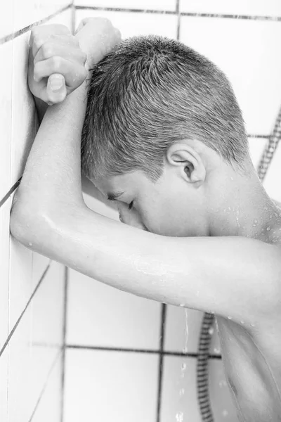 Side view of sad boy leaning on wall in shower — Stockfoto