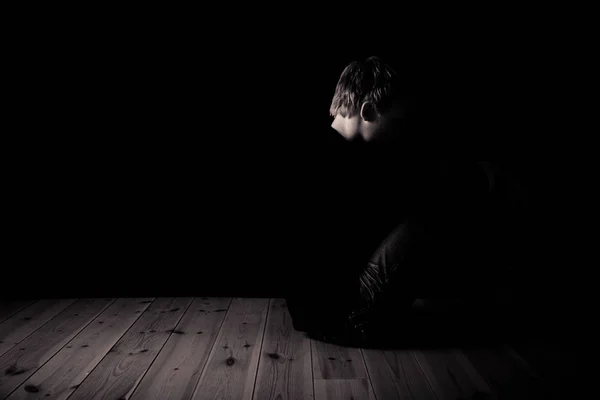 Young teenage boy sitting in darkness in an attic — Stock Photo, Image