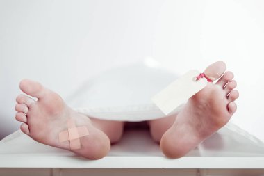Boy lying on a mortuary slab with a tag on his toe clipart