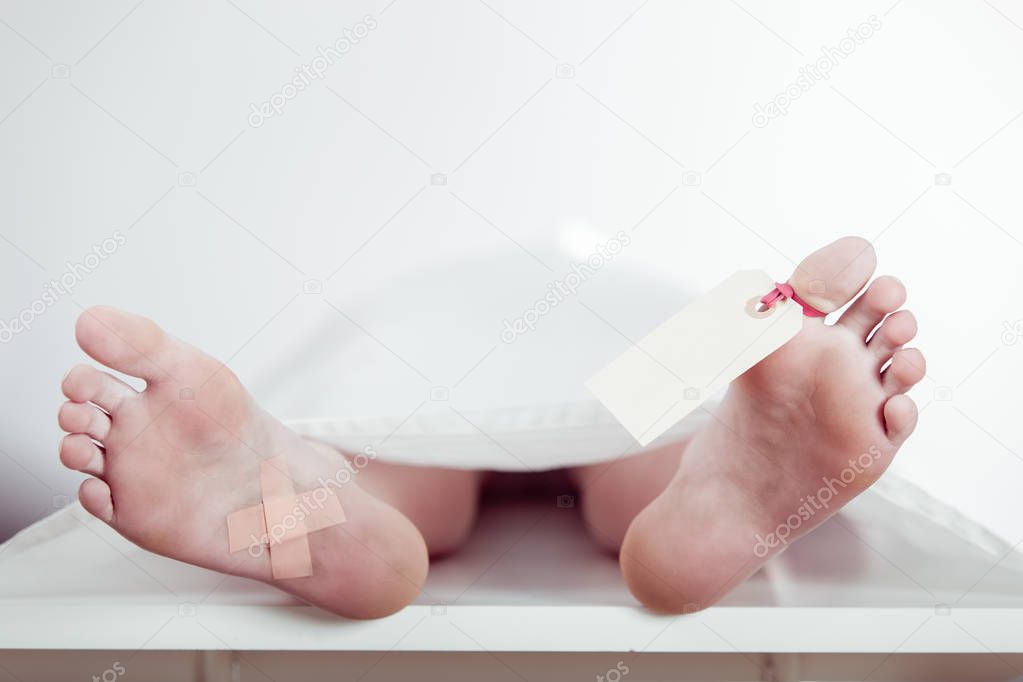 Boy lying on a mortuary slab with a tag on his toe