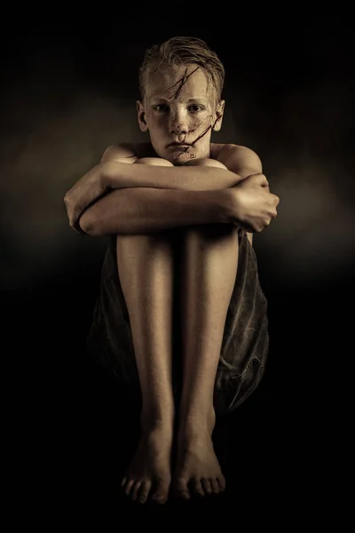 Getraumatiseerde jongen zit met armen rond zijn knieën — Stockfoto