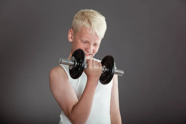 Boy curling a dumbbell over gray background Stock Picture