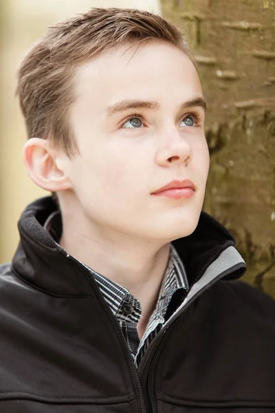 Thoughtful boy leans against trunk of tree Stock Picture