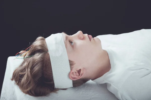 Мальчик лежит с повязкой, обернутой вокруг головы — стоковое фото