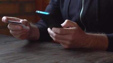 Siyah kapüşonlu bir iş adamı. Kredi kartı ve akıllı telefonla online alışveriş yapıyor.