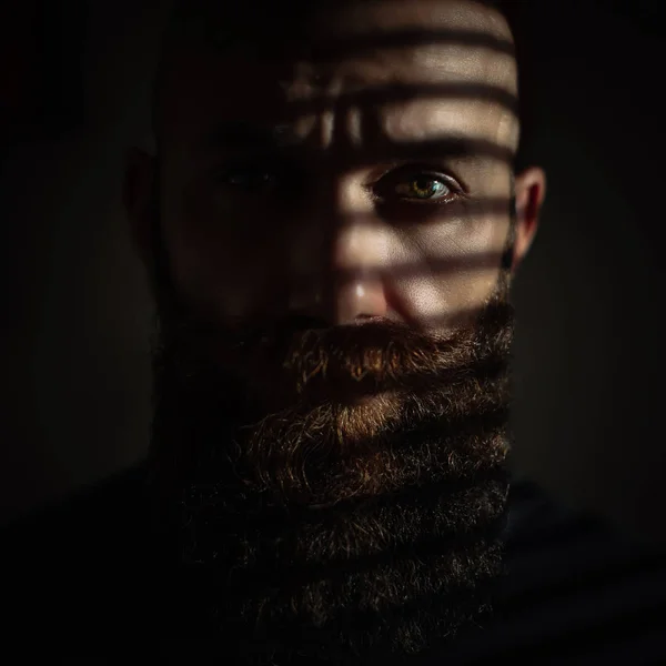 Close-up portrait of middle aged brutal bearded man with expressive eyes and striped shadows on his face — 스톡 사진
