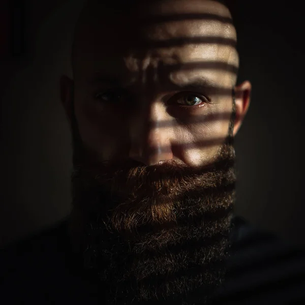 Close-up portrait of middle aged brutal bearded man with expressive eyes and striped shadows on his face — 스톡 사진