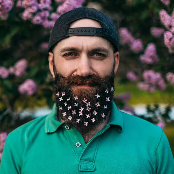 Un hombre barbudo con una barba decorada con flores lila para las vacaciones de primavera — Foto de Stock