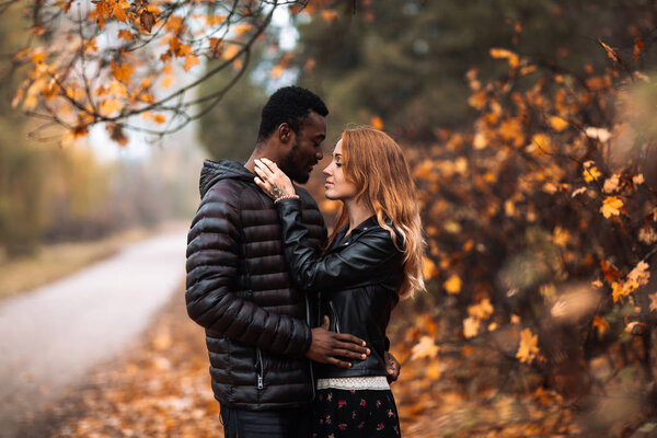Межрасовая пара позирует в расплывчатом осеннем парке
