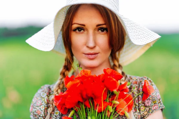 Porträtt av vacker rödhårig kvinna i hatt på grönt fält med bukett vallmo — Stockfoto