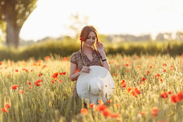 Redhead woman with hat on green field with poppies