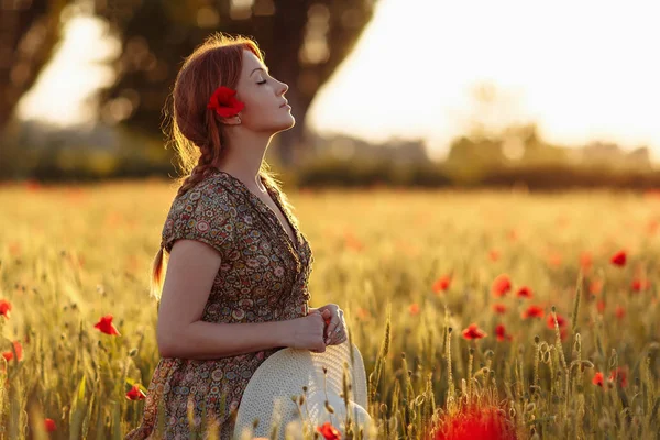 Redhead woman with hat on green field with poppies