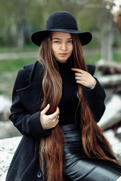 Jovem bela mulher na moda em chapéu preto com cabelos longos posando no fundo embaçado — Fotografia de Stock