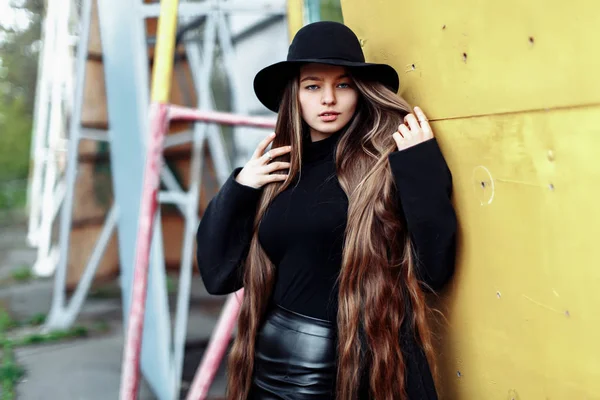 Jovem bela mulher na moda em chapéu preto com cabelos longos posando no fundo embaçado — Fotografia de Stock