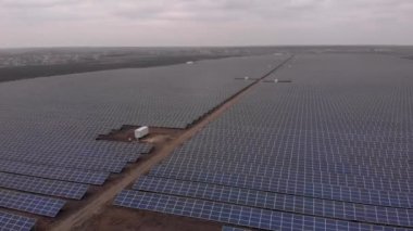 Hava aracı bulutlu bir sonbahar gününde güneş çiftliğindeki büyük güneş panellerine doğru bakıyor. Güneş pili santralleri. görüntüler 4k.