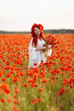 Yeşil tarlada çelenk takmış güzel kızıl saçlı kadın ve bir buket gelincik.