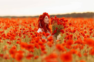 Yeşil tarlada çelenk takmış güzel kızıl saçlı kadın ve bir buket gelincik.