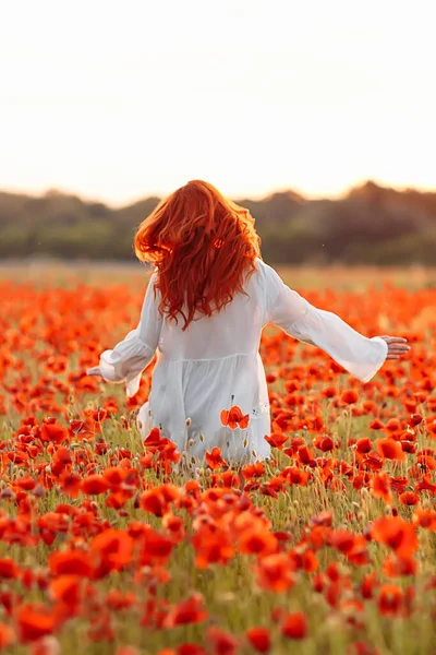 Mulher feliz ruiva sorrindo em vestido branco no campo de papoilas no pôr do sol de verão — Fotografia de Stock