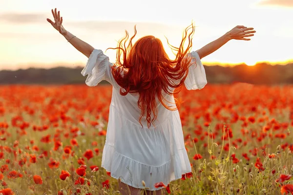 Mulher feliz ruiva sorrindo em vestido branco no campo de papoilas no pôr do sol de verão — Fotografia de Stock