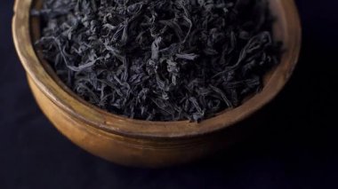 Kapatın, siyah çay yaprakları siyah arka planda kilden bir kasede dönüyor. Kavram - Geleneksel Çin Çayı