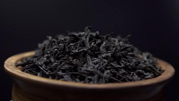 Primer plano ver las hojas secas de té negro rotar en un tazón de barro sobre fondo negro. Concepto - Té chino tradicional — Vídeos de Stock