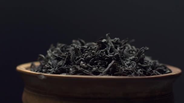 Vue rapprochée feuilles de thé noir sec tourner dans un bol d'argile sur fond noir. Concept - Thé chinois traditionnel — Video