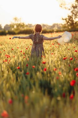 Beyaz şapkalı güzel kızıl kadın yeşil tarlada gelinciklerle poz veriyor.