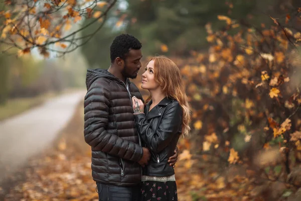 Interracial couple posing in blurry autumn park background, black man and white redhead woman