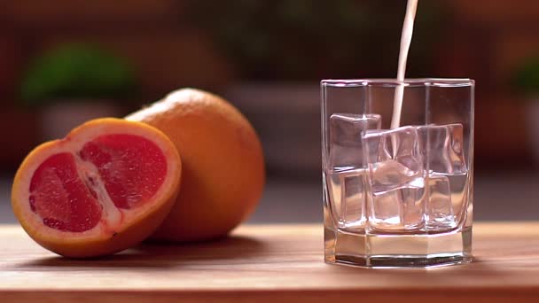 Verse grapefruitsap dat in een doorzichtig glas met ijs wordt gegoten. Snijd grapefruits op een tafel. Gezond levensstijl concept. — Stockvideo