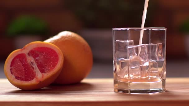 Frischer Grapefruitsaft, der in ein transparentes Glas mit Eis gegossen wird. Grapefruits in Scheiben geschnitten auf einem Tisch. Gesunder Lebensstil. — Stockvideo