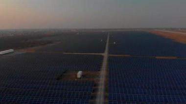 Parlak günbatımında güneş çiftliğindeki büyük güneş panellerine hava aracı görüntüsü. Güneş pili santralleri. görüntüler 4k.