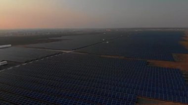 Parlak günbatımında güneş çiftliğindeki büyük güneş panellerine hava aracı görüntüsü. Güneş pili santralleri. görüntüler 4k.