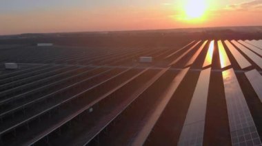 Parlak günbatımında güneş çiftliğindeki büyük güneş panellerine hava aracı görüntüsü. Güneş pili santralleri. görüntüler 4k.