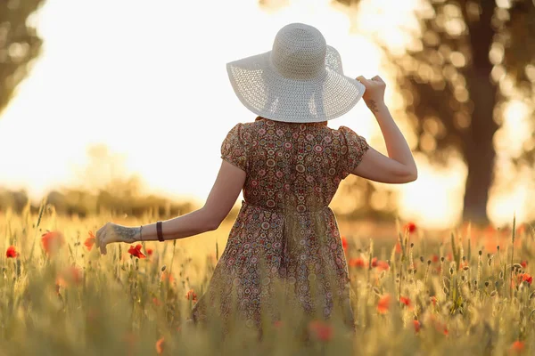 Redhead woman in white hat on green field with poppies in summer sunset