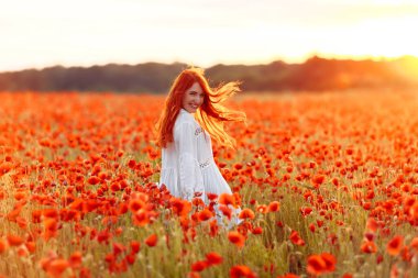 Sıcak yaz günbatımında haşhaş tarlasında gülümseyen beyaz elbiseli mutlu kadın.