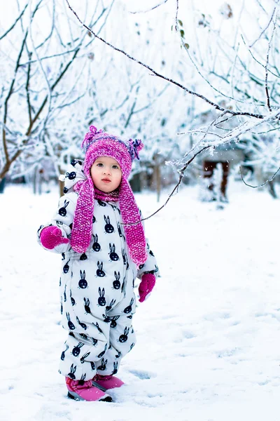 Enfant par temps neigeux. Bébé fille en blanc snowsuite et chapeau rose, bottes gants dans le parc d'hiver de neige . — Photo