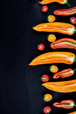 Yarım kırmızı ve sarı biber yeşil dal kiraz domates siyah arka plan üzerine yakınındaki karışık. Üstten Görünüm. Çerçeve. Kopya alanı.