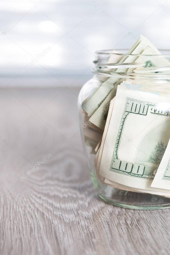 Money. Dollars in open jar on grey wooden background.  Copy space.