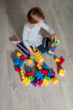 Eğlenceli ve parlak plastik inşaat blokları inşa sahip tanınmaz kız çocuk. Yürümeye başlayan çocuk yerde oynuyor. Oyuncaklar geliştirilmesi. Erken öğrenme. Üstten Görünüm.