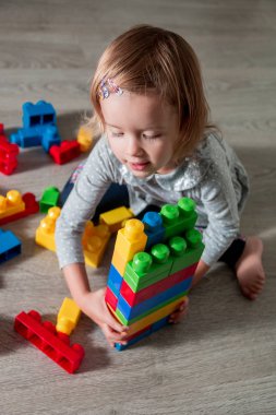 Eğlenceli ve parlak plastik inşaat blok yapı olan kız çocuk. Yürümeye başlayan çocuk yerde oynuyor. Oyuncaklar geliştirilmesi. Erken öğrenme.