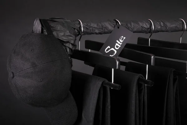 出售标志。黑色的帽子，裤子，牛仔裤挂在衣服上机架背景。星期五。关闭. — 图库照片