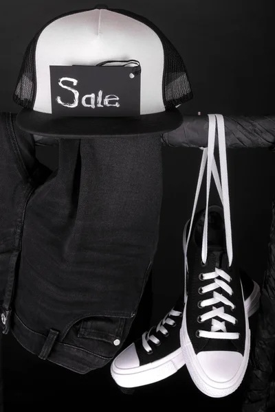 Försäljning tecken. Svarta och vita sneakers, cap byxa, jeans hängande på kläder rack bakgrund. fredag. Närbild. — Stockfoto