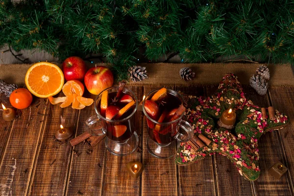 クリスマスにホットワインの果物と木製のテーブルの上のスパイス。バック グラウンドでのクリスマス装飾です。2 つのグラス。周りのレシピ食材を飲んで冬の温暖化. — ストック写真