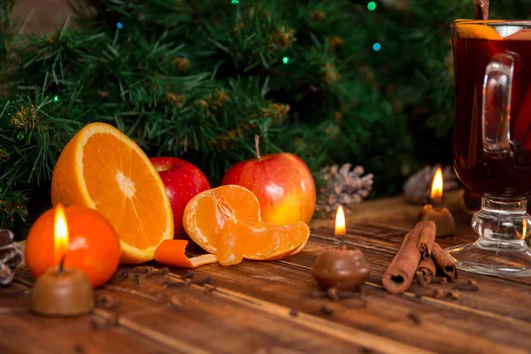 Gyertyák, gyümölcsök és fűszerek, a fából készült asztal, forralt bor mellett. Karácsonyi díszek a háttérben. Új év. — Stock Fotó