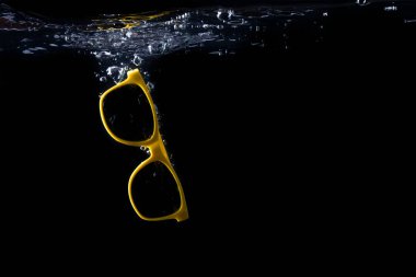 Siyah arka plan üzerine su içine sıçramasına sarı güneş gözlüğü. gözlük düşüyor. Kopya alanı.