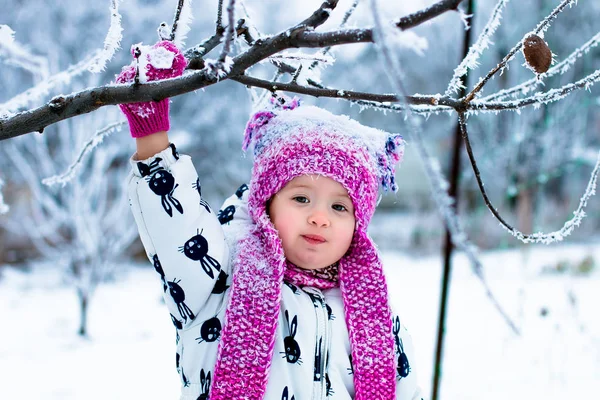 Enfant par temps neigeux. Bébé fille en suite blanche et chapeau rose, bottes gants dans le parc d'hiver de la neige. Heureux . — Photo